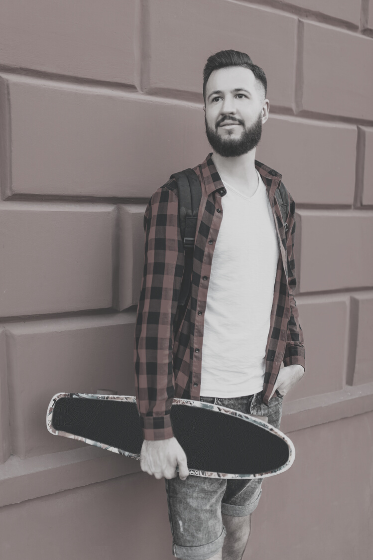 guy with a beard on a background of a brick empty wall with a skateboard