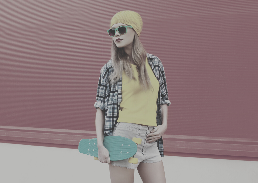 cool blonde woman with skateboard wearing colorful yellow hat on pink background